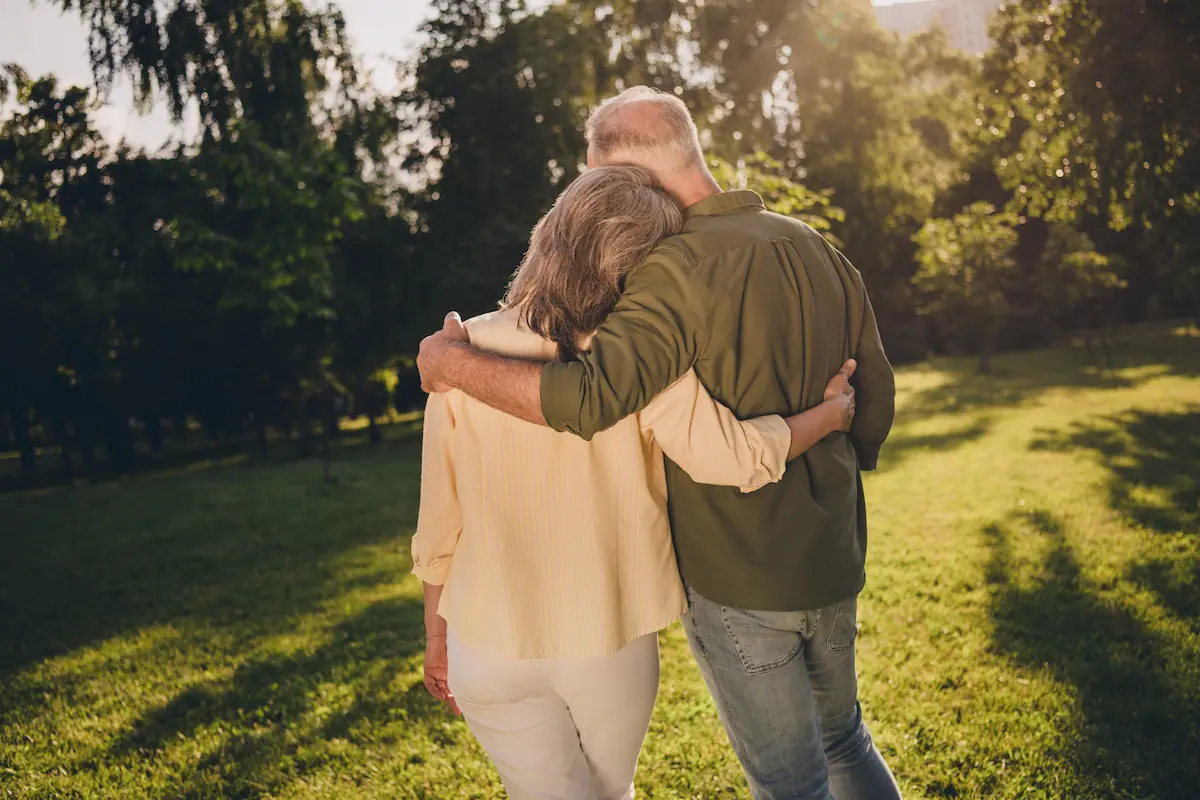 Older couple embracing in a sunlit garden while looking toward their future
